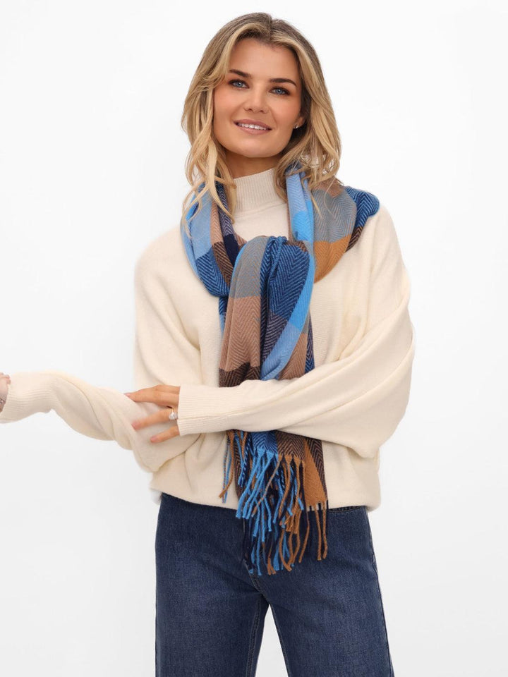 Woman wearing a cream sweater and blue plaid scarf on a white background