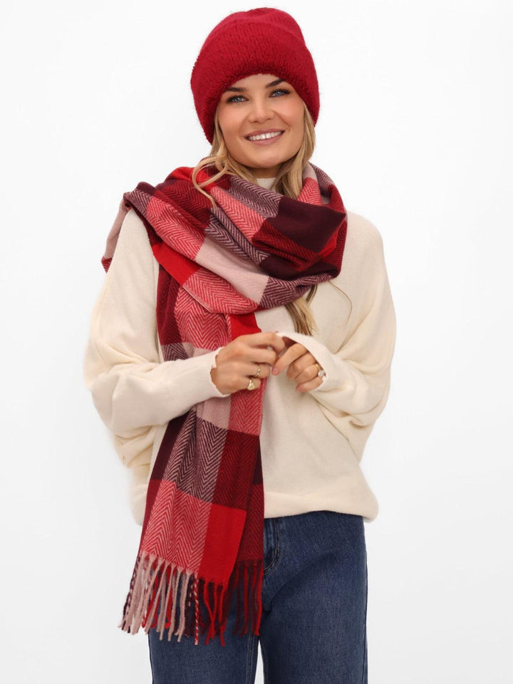 Woman wearing a red checkered scarf, red beanie, and white sweater on a white background