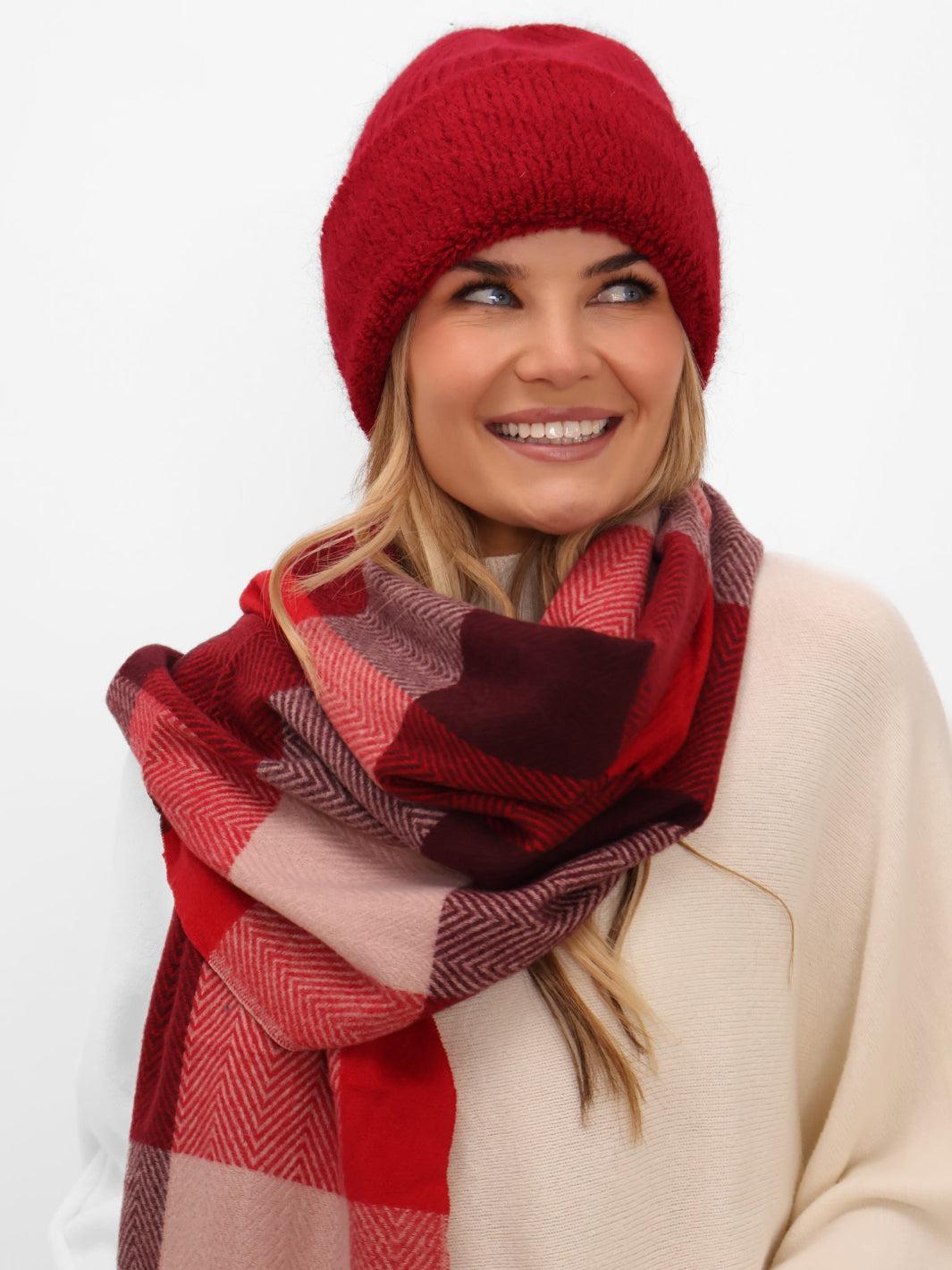 Woman wearing a red knit beanie and a red and pink checkered scarf on a white background