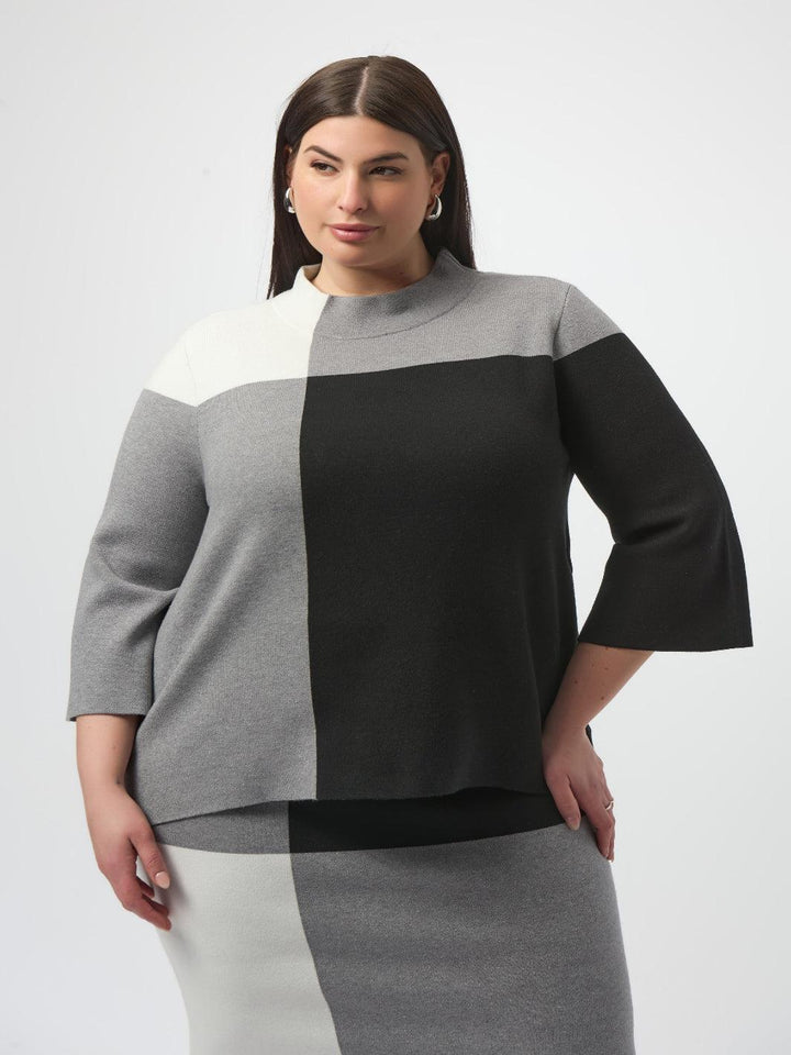Woman wearing a color-blocked sweater with gray, black, and white sections on a white background
