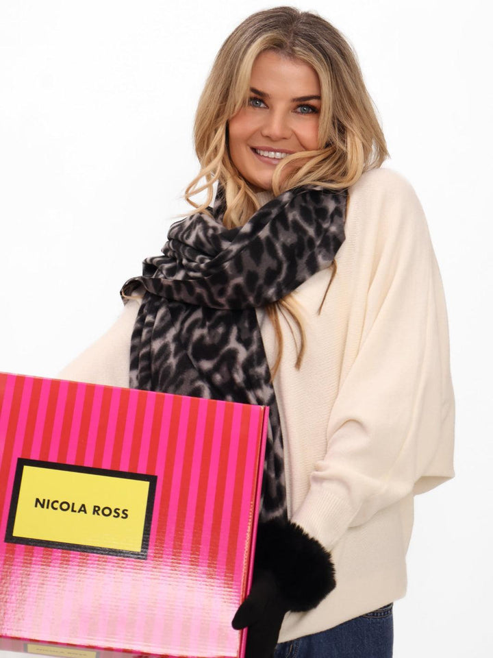 Woman holding a pink bag with 'Nicola Ross' branding, wearing a leopard print scarf and black gloves.