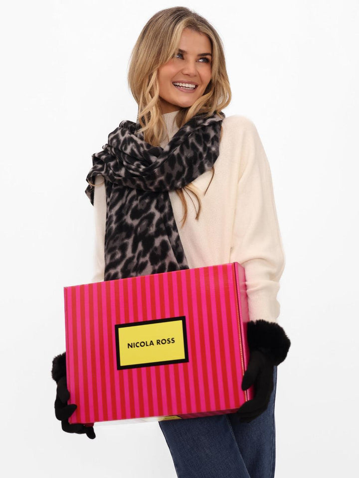 Woman holding a pink striped box with 'Nicola Ross' branding, wearing a leopard print scarf and black gloves.