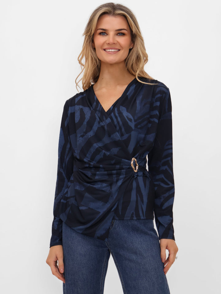 Woman wearing a navy patterned top and jeans on a white background