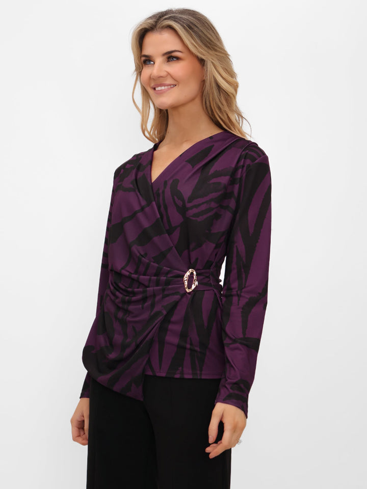 Woman wearing a purple patterned top with a belt on a white background