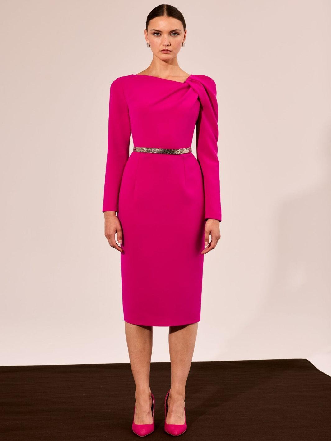 Woman wearing a bright pink dress with a silver belt against a beige background