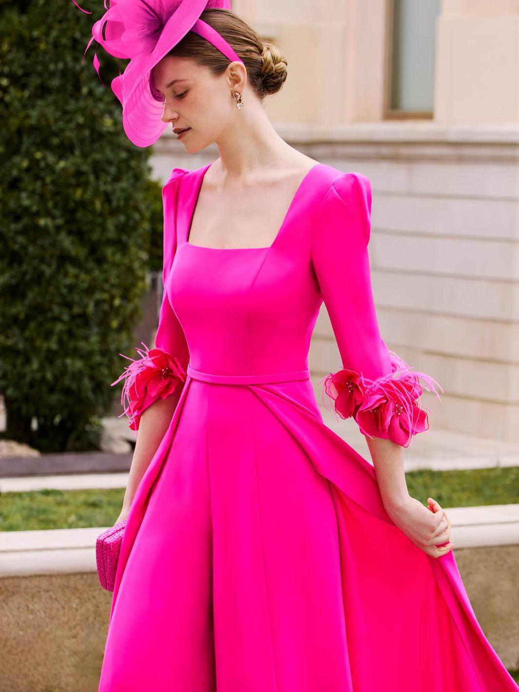 Woman wearing a bright pink dress with floral details outdoors.