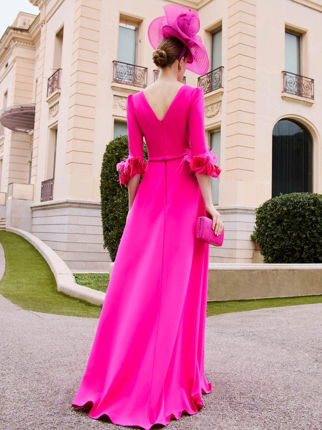 Woman in a bright pink dress and hat standing in front of an elegant building.