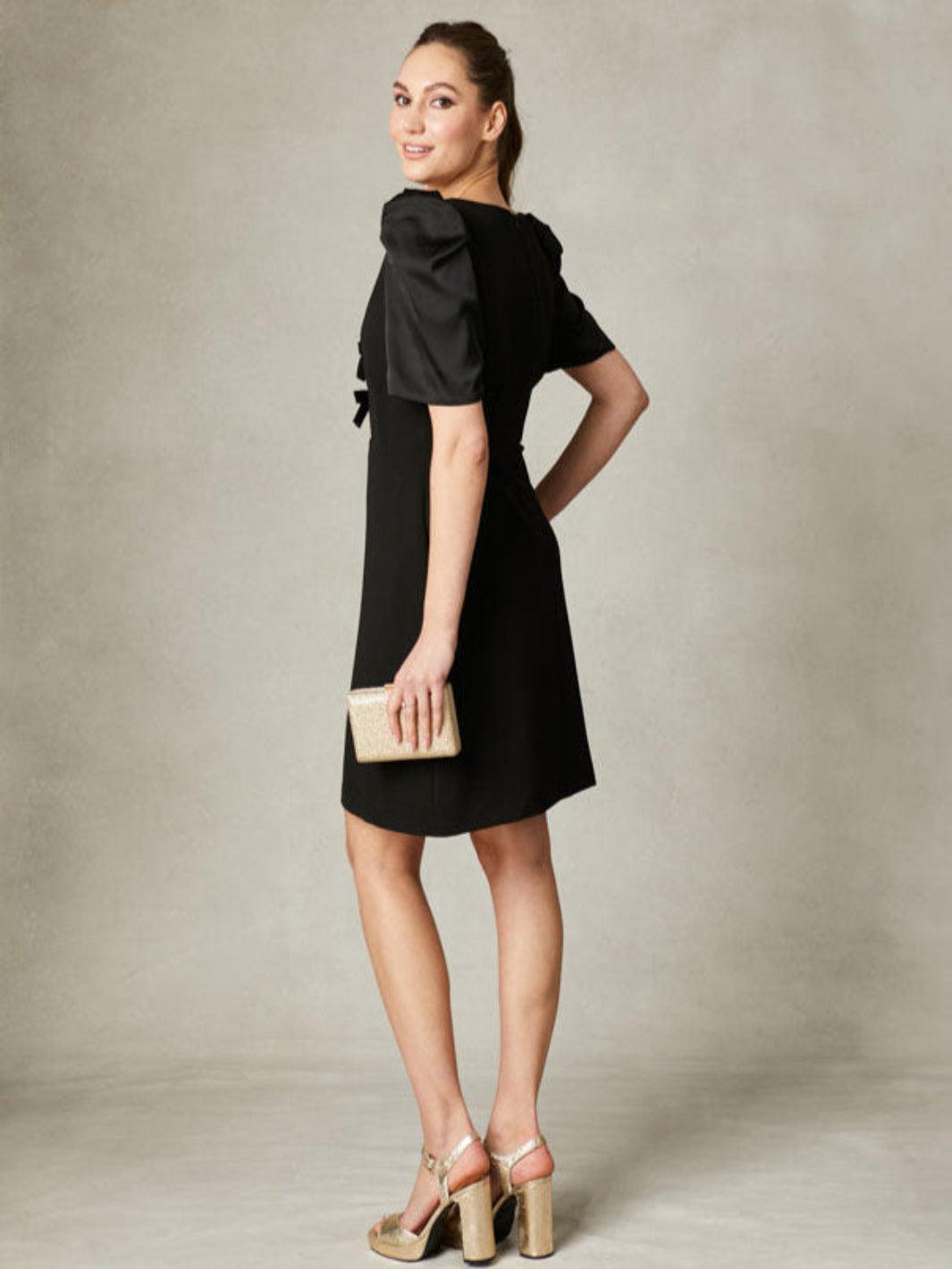 Woman wearing a black dress with a bow detail on a plain background