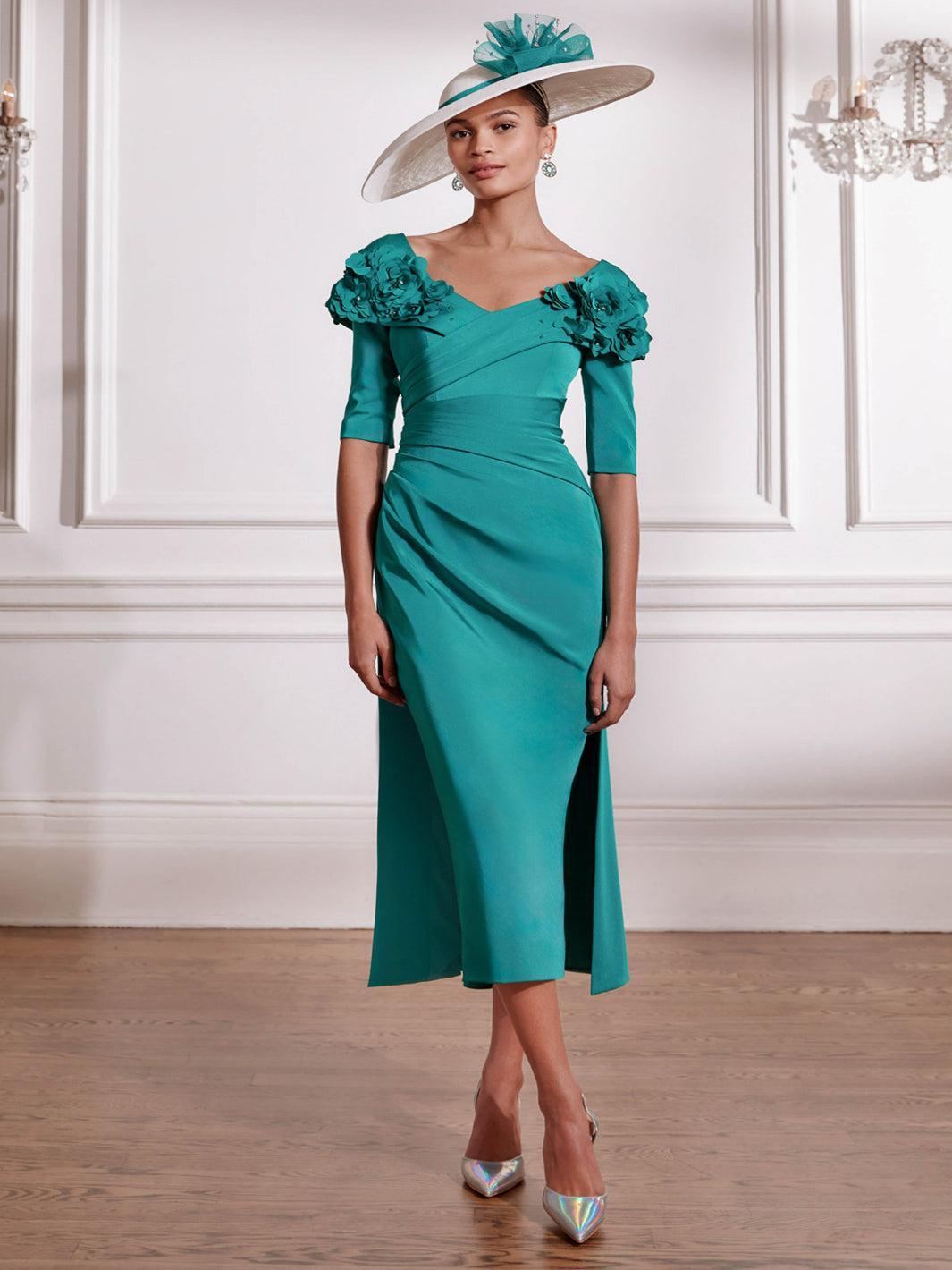 Woman wearing a teal dress with floral shoulder details and a matching hat indoors.