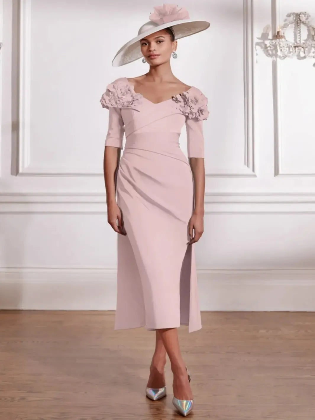 Woman wearing a light pink dress with floral details and a matching hat in an elegant interior setting.