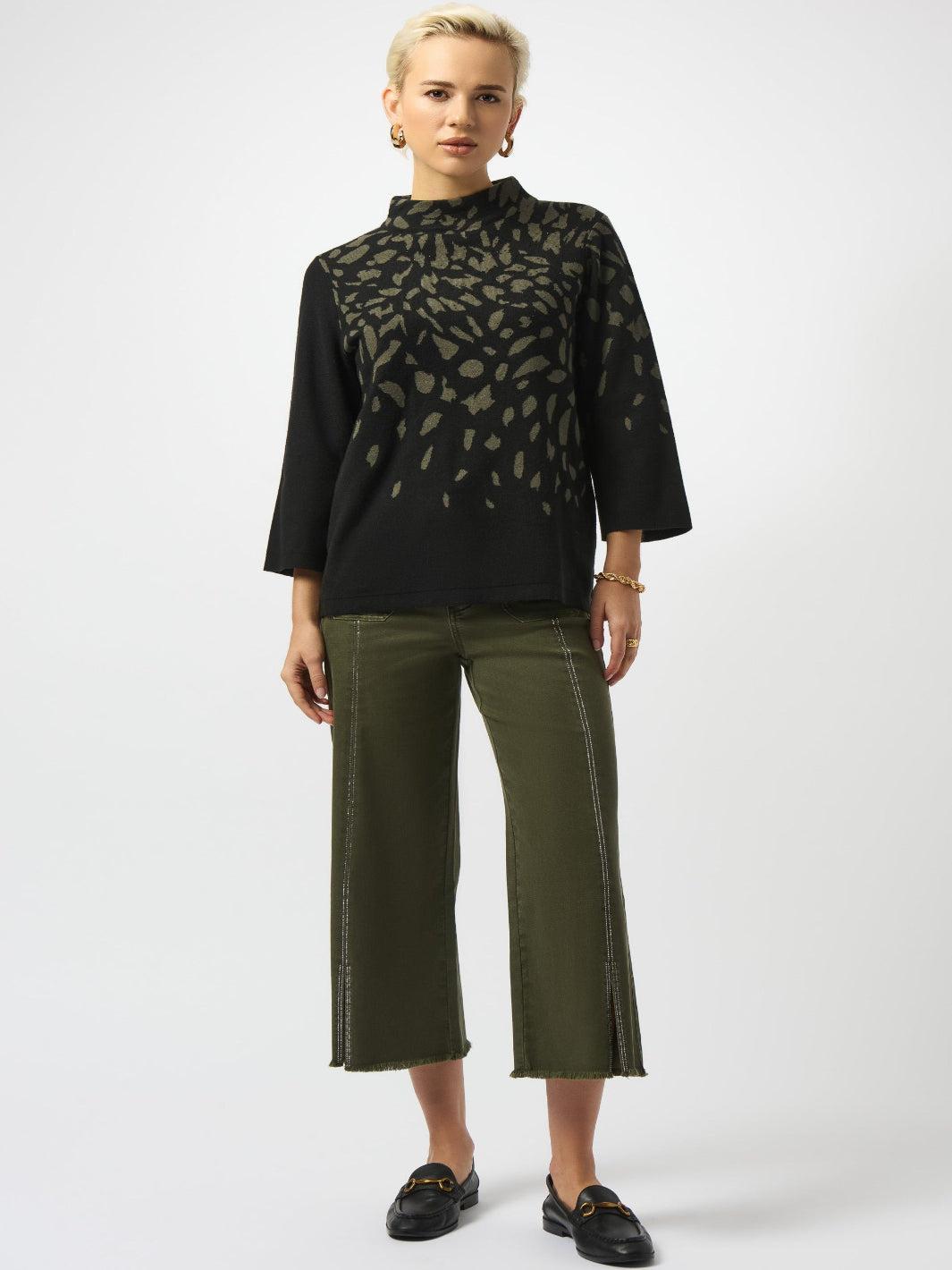Woman wearing a black patterned blouse and green pants on a white background