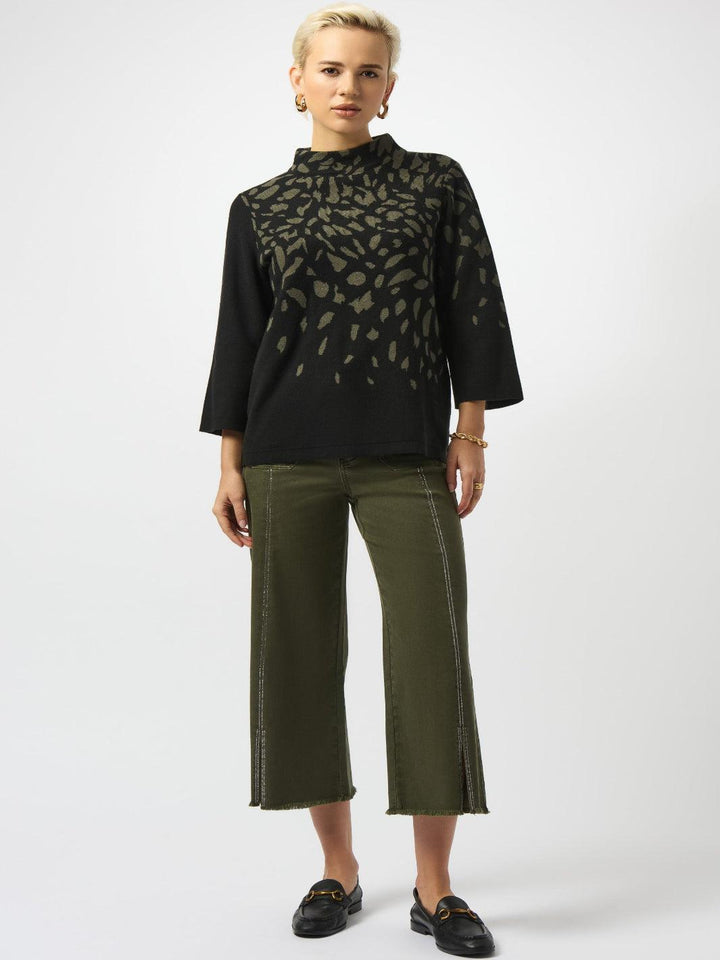 Woman wearing a black patterned blouse and green pants on a white background