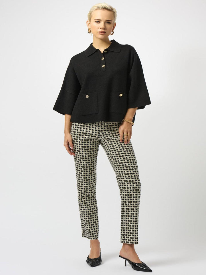 Woman wearing a black blouse with gold buttons and patterned pants on a white background
