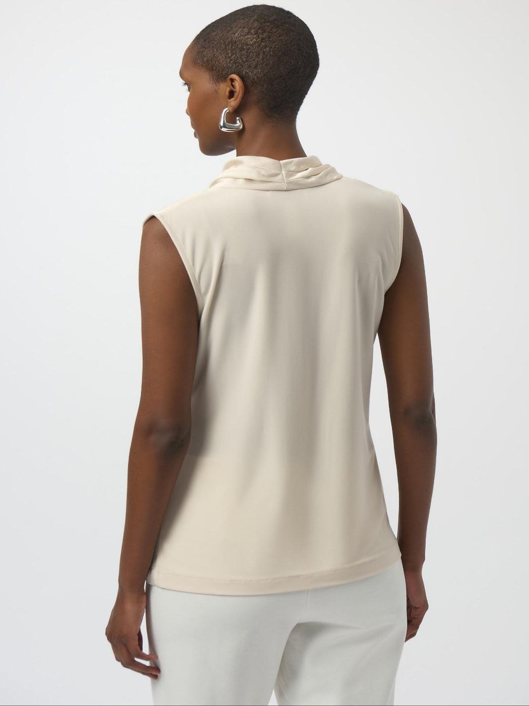 Woman wearing a beige sleeveless top and white pants on a light gray background