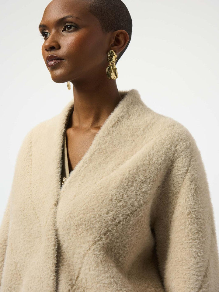 Woman wearing a beige cardigan with gold earrings on a white background