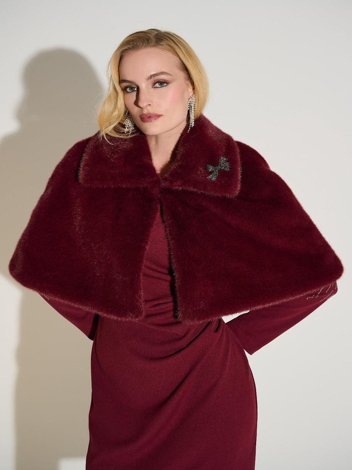 Woman wearing a burgundy fur stole over a red dress against a white background