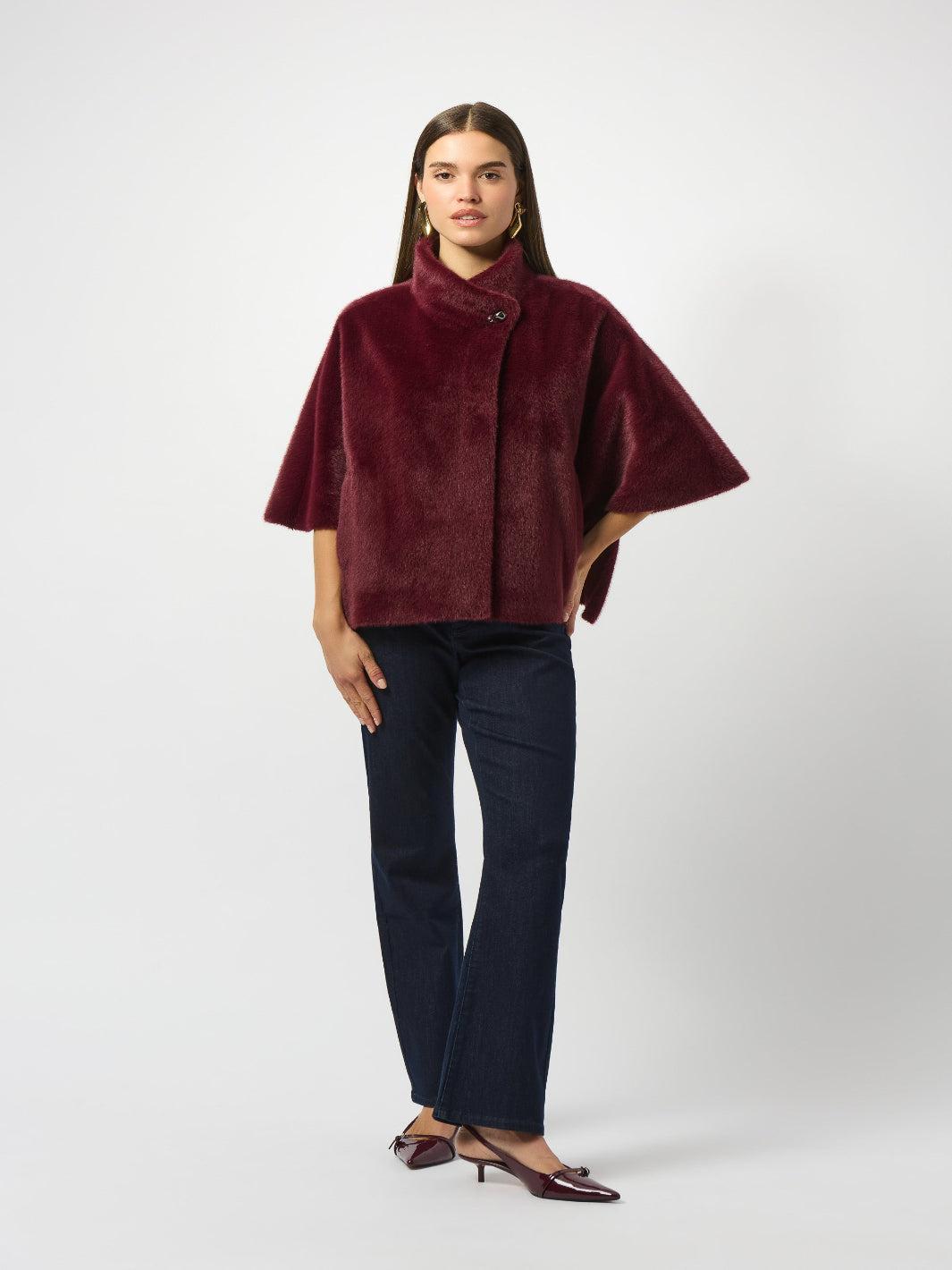 Woman wearing a burgundy cape over a dark outfit on a white background
