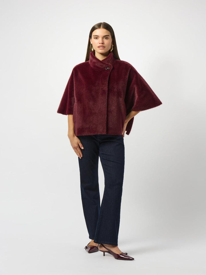 Woman wearing a burgundy cape over a dark outfit on a white background