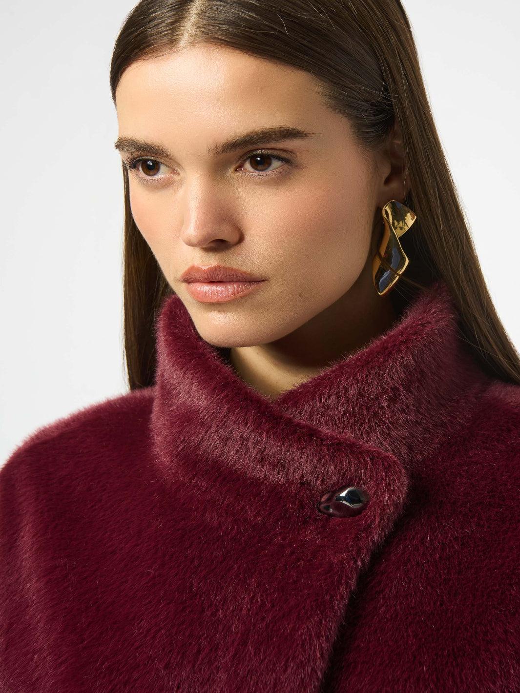 Close-up of a person wearing a burgundy coat with a plain background