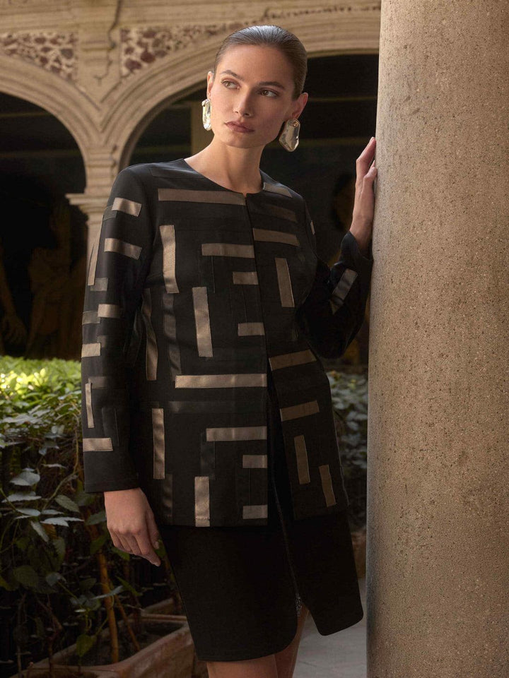 Woman wearing a patterned coat in an outdoor setting with architectural elements.