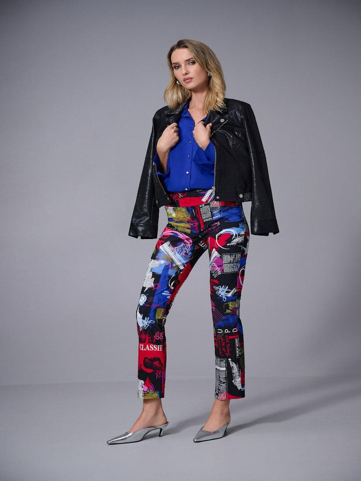 Woman wearing a black leather jacket, blue shirt, and colorful patterned pants on a gray background