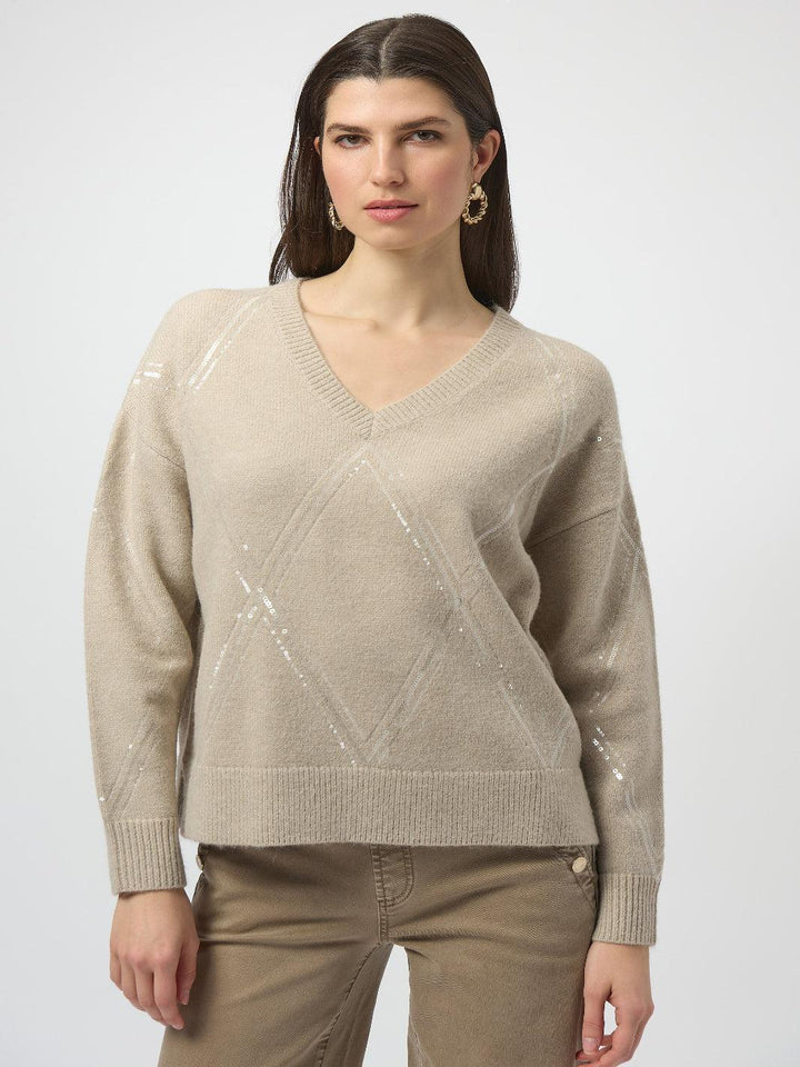 Woman wearing a beige sweater with a subtle pattern on a white background