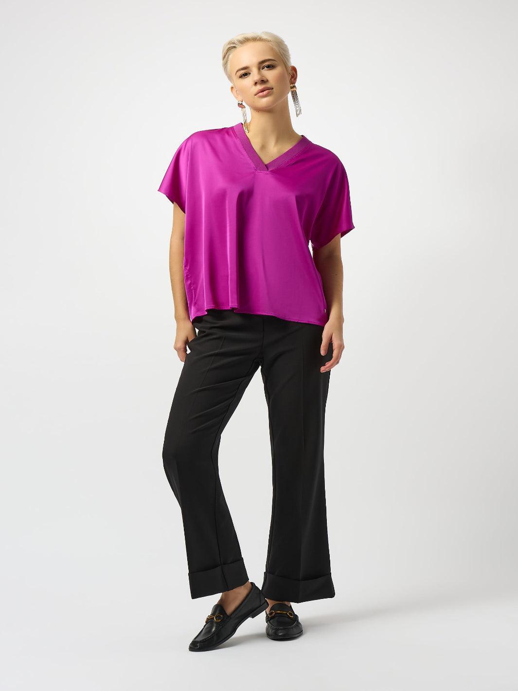Person wearing a bright pink top and black pants on a white background
