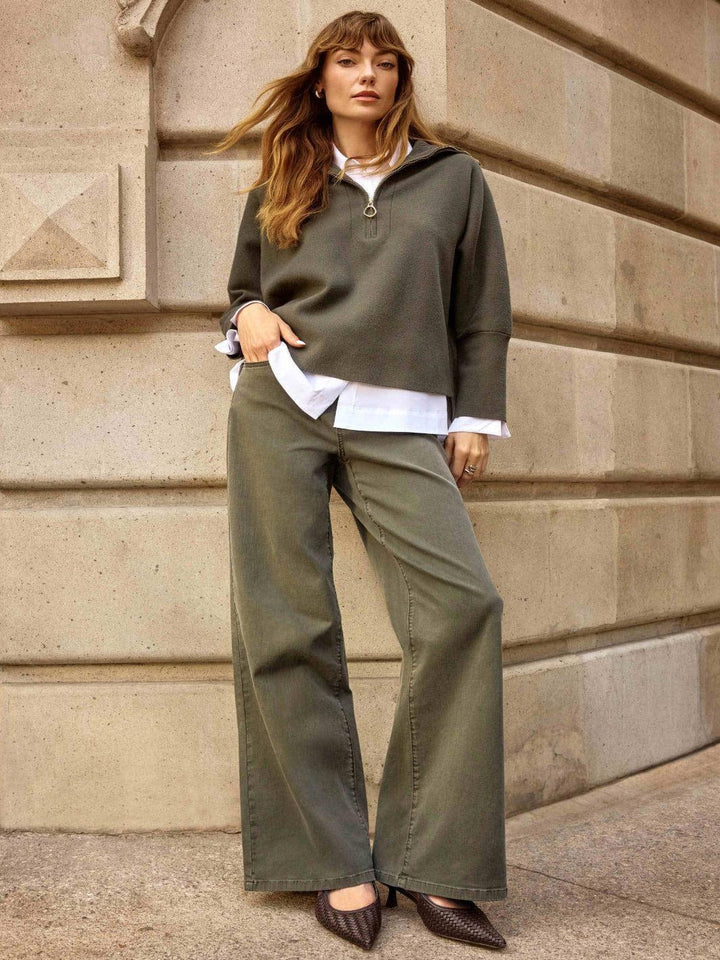 Woman in olive green outfit standing against a stone wall