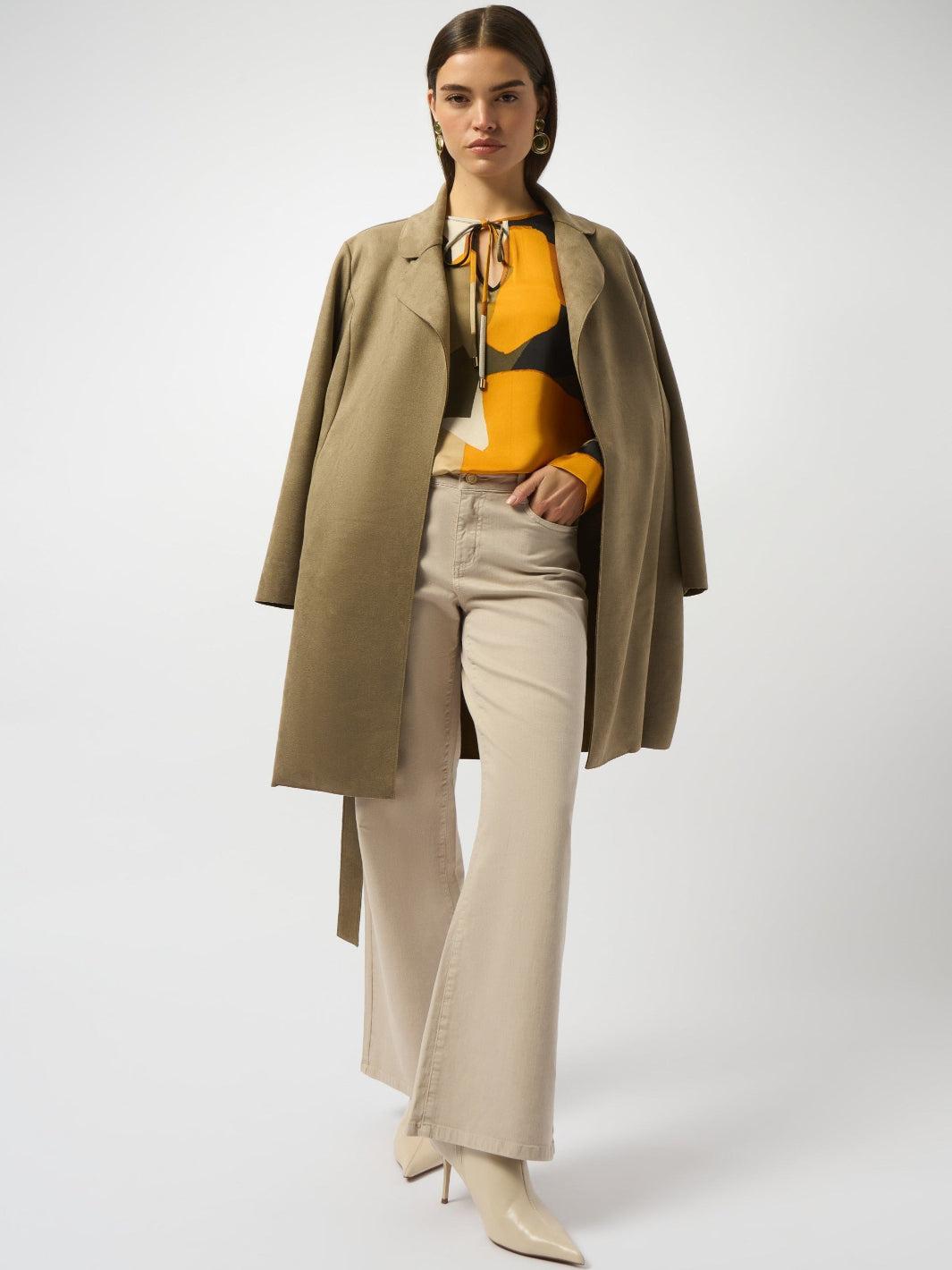 Woman wearing a beige coat, yellow top, and beige pants on a white background