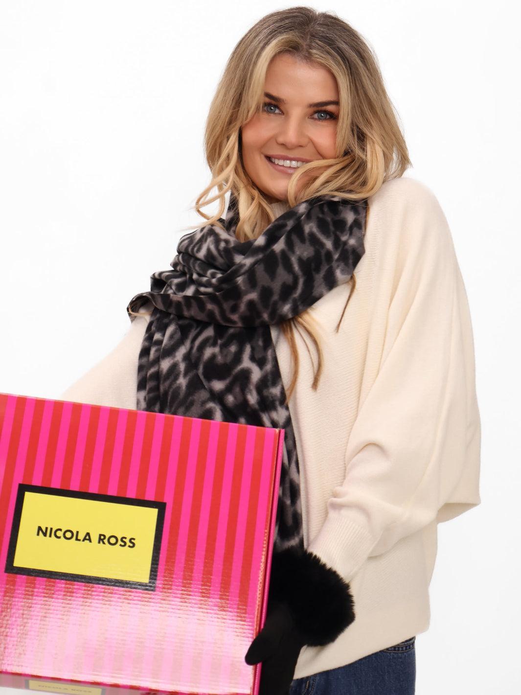 Woman holding a pink bag with 'Nicola Ross' branding, wearing a leopard print scarf and black gloves.