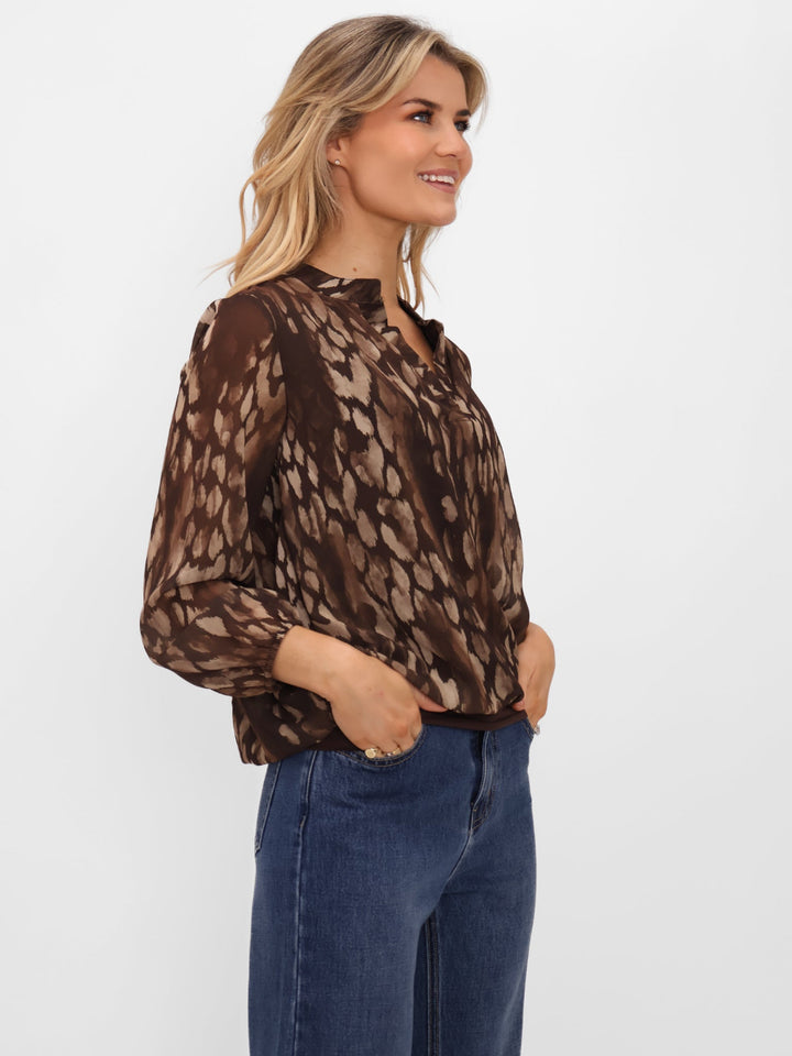Woman wearing a brown patterned blouse and blue jeans on a white background