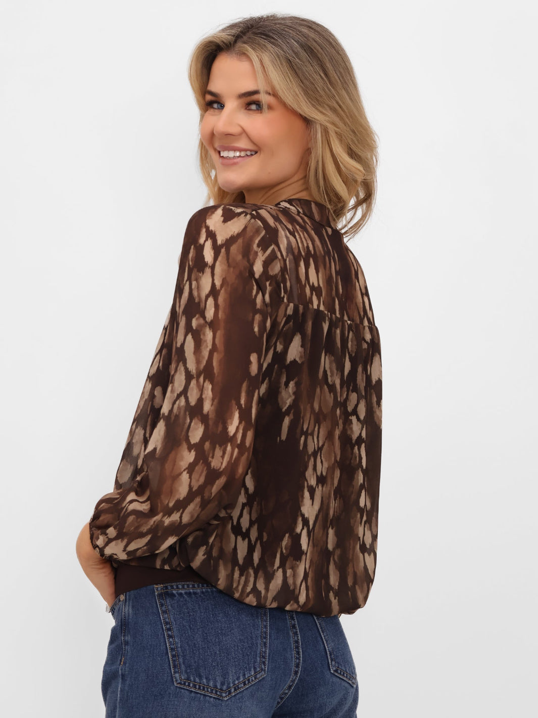 Woman wearing a brown patterned blouse and blue jeans on a white background