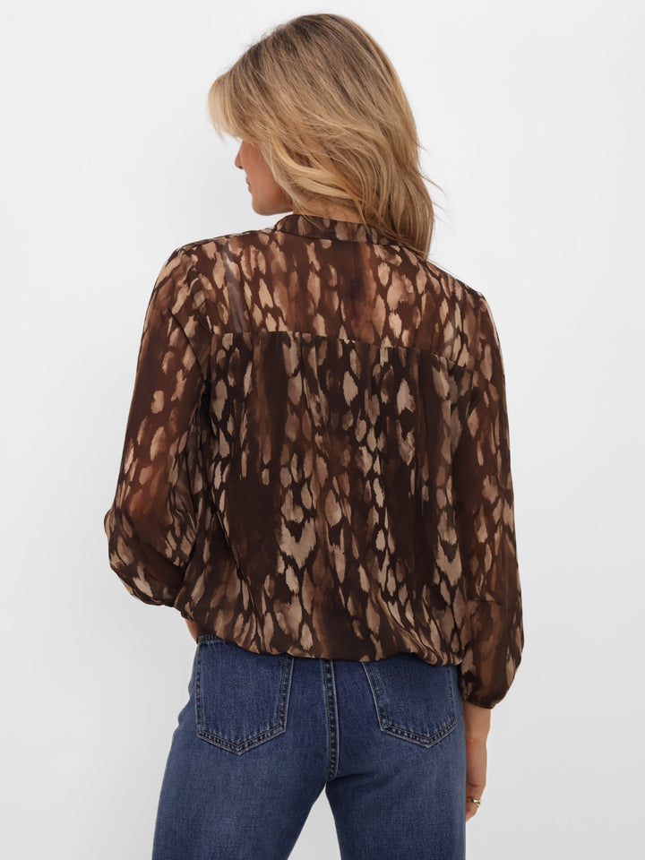Person wearing a brown patterned blouse and blue jeans on a white background