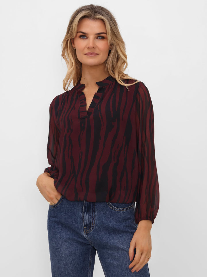 Woman wearing a burgundy and black striped blouse with blue jeans on a white background