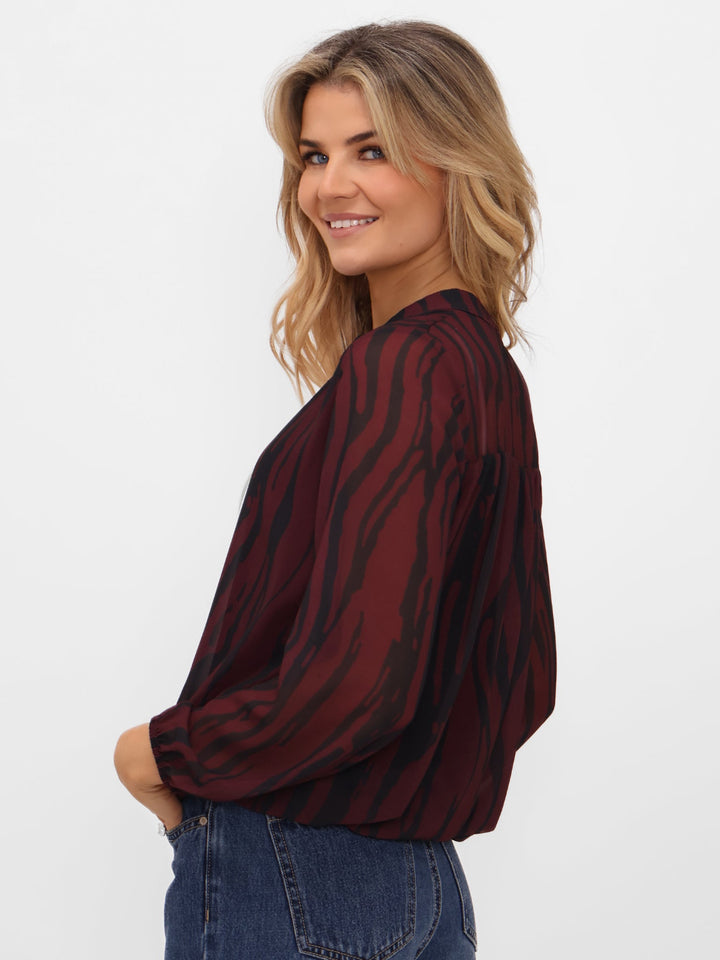 Woman wearing a burgundy and black striped blouse with blue jeans on a white background