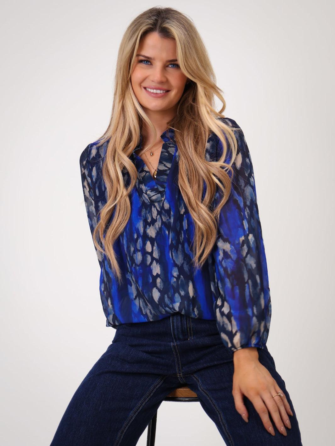 Woman wearing a blue patterned blouse and dark jeans on a white background