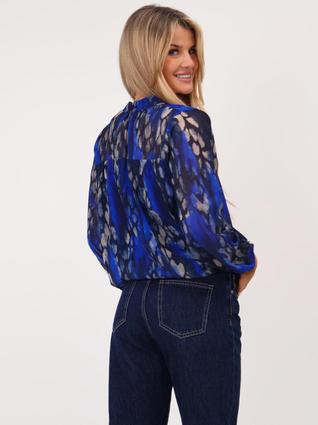 Woman wearing a blue patterned blouse and dark jeans on a white background