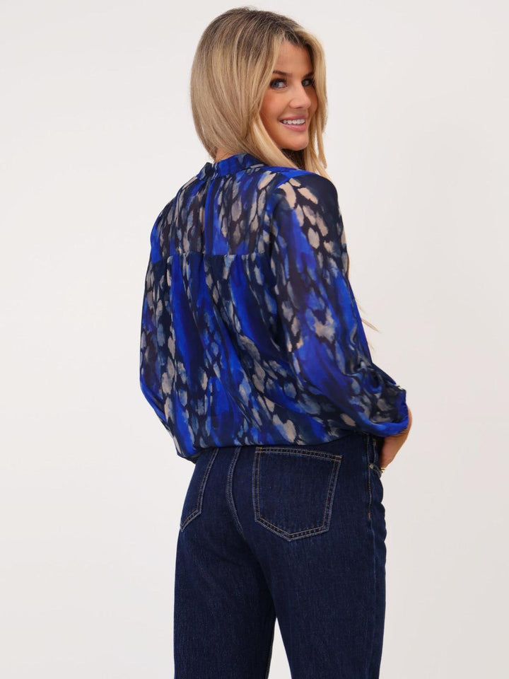 Woman wearing a blue patterned blouse and dark jeans on a white background