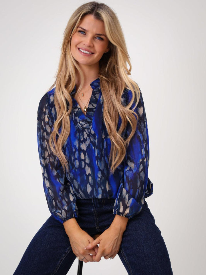 Woman wearing a blue patterned blouse and dark jeans on a white background