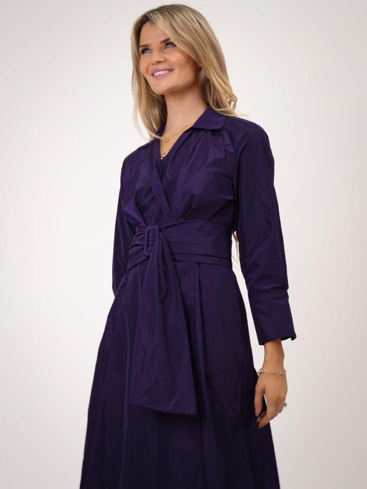 Woman wearing a purple dress with a belt against a white background