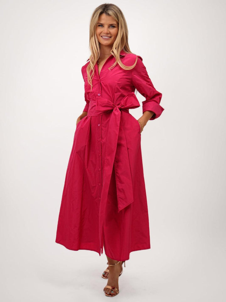 Woman wearing a bright pink dress with a belt on a white background