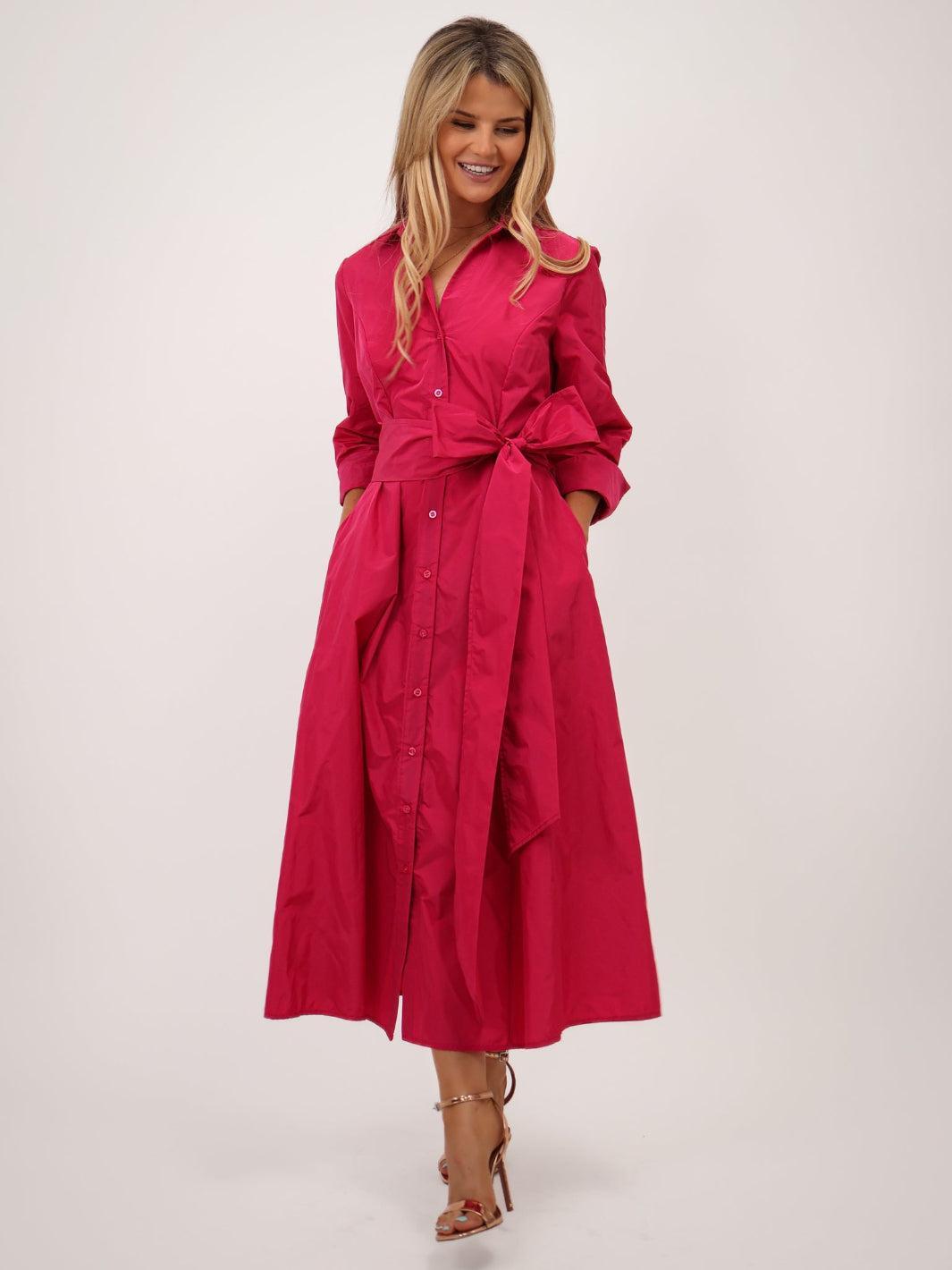 Woman wearing a bright pink dress with a belt on a white background