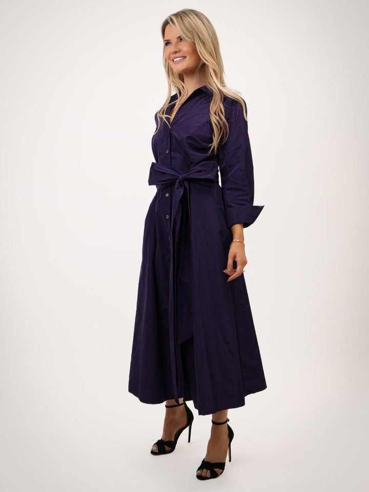 Woman wearing a long dark purple dress with a belt on a white background