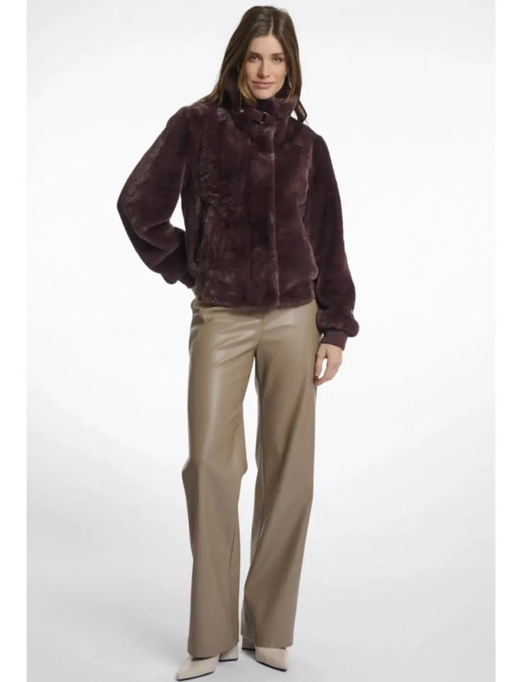 Woman wearing a brown fur jacket and beige pants on a white background