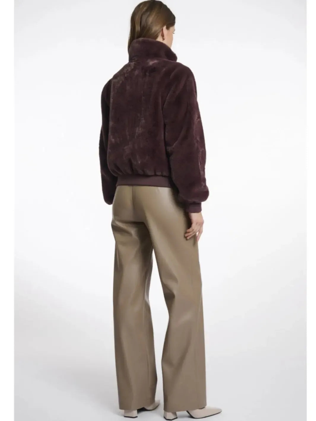 Person wearing a brown fur jacket and beige pants on a white background