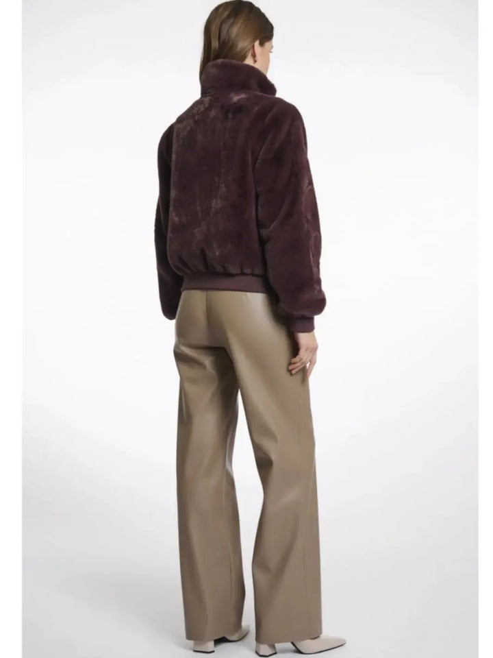 Person wearing a brown fur jacket and beige pants on a white background