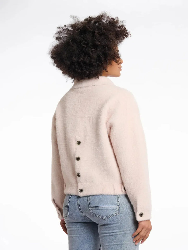 Person wearing a beige jacket with black buttons on a white background