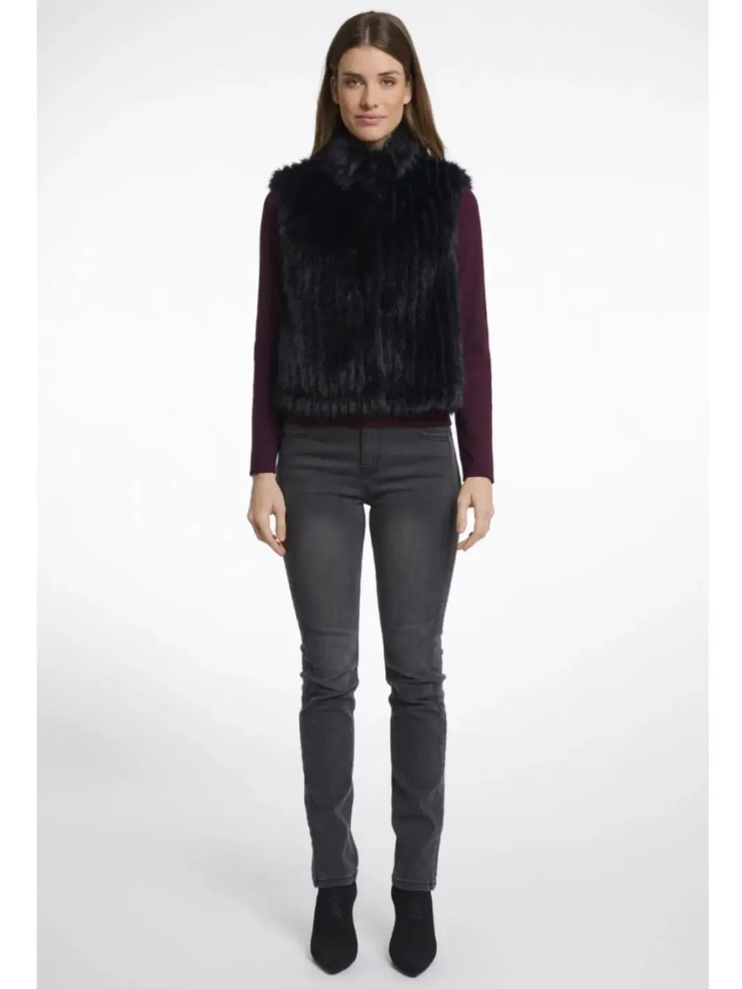 Woman wearing a dark fur vest over a purple top with gray pants on a white background