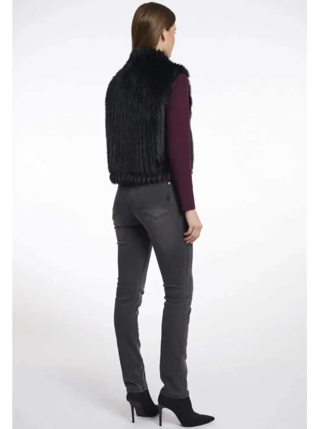 Person wearing a black fur vest, purple top, gray jeans, and black high-heeled shoes on a white background