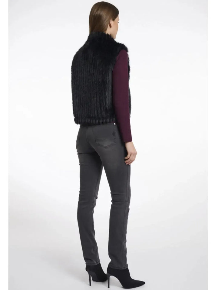 Person wearing a black fur vest, purple top, gray jeans, and black high-heeled shoes on a white background